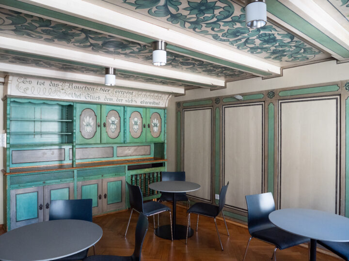 Die Grüne Stube hat Fischgrätenparkett, einen grünen Kachelofen und grüne Wand- und Deckenverzierungen und ist mit runden Tischen mit jeweils drei Stühlen ausgestattet.